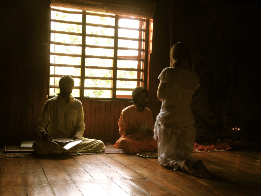 Silhouetted students being taught meditation in a dark room in front of window.