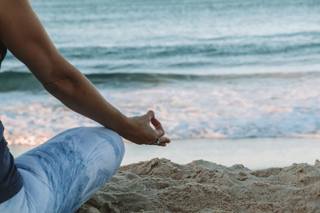 Person meditating on the beach with rolling waves in the background.