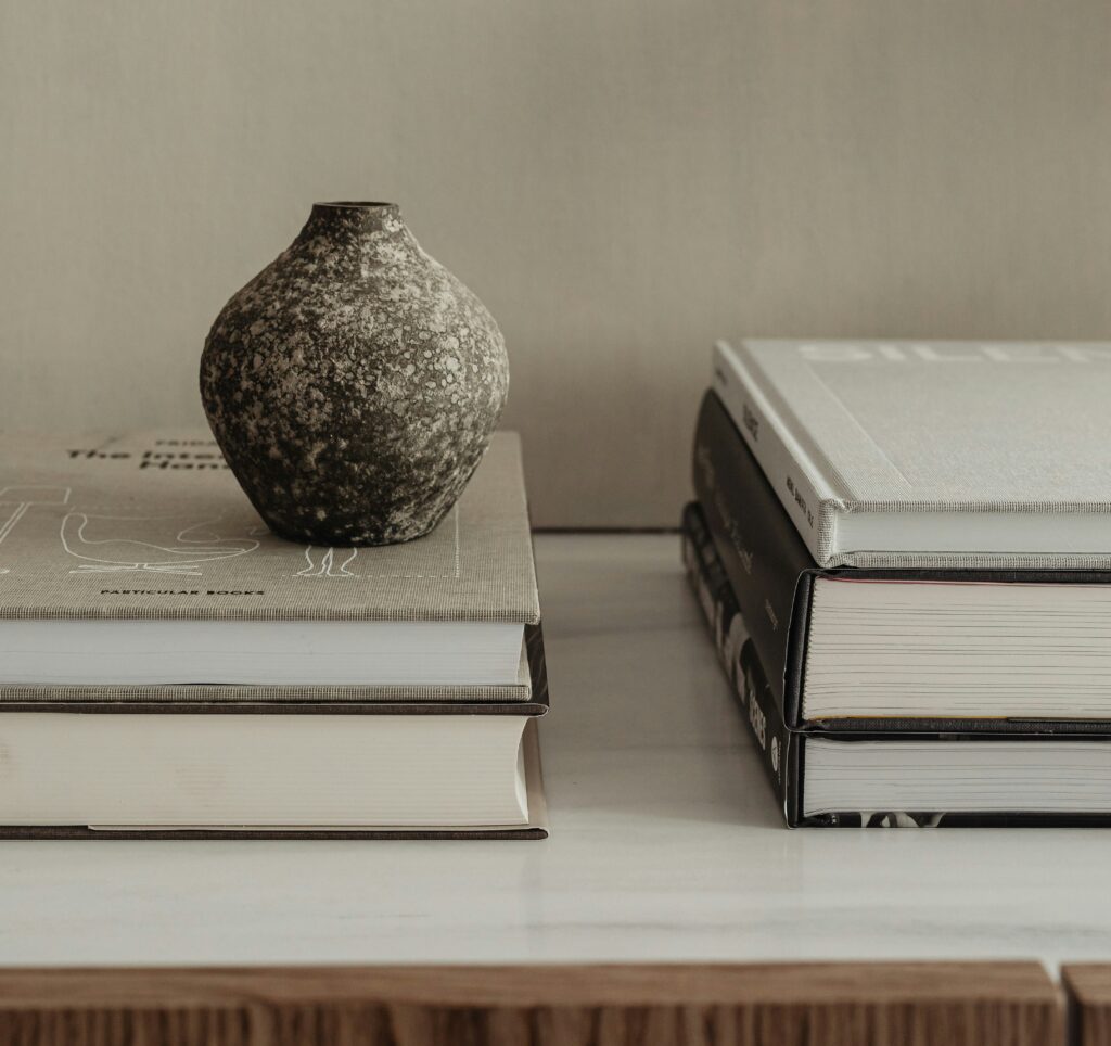 Ceramic vase sitting atop a stack of books next to a second stack of books.