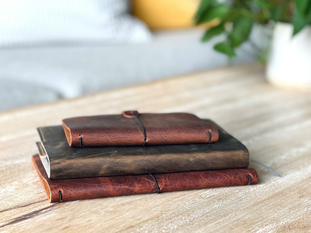 Three leather journals stacked on a wooden table.