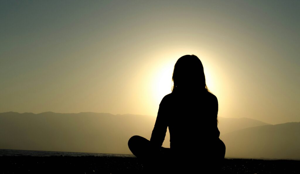 Person sitting on the ground in front of a sunset.