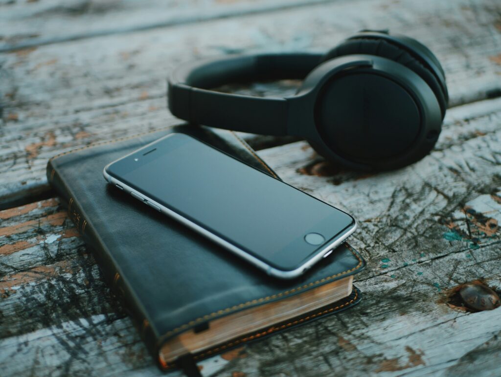 Headphones, an iPhone, and a leather book on a wooden table.