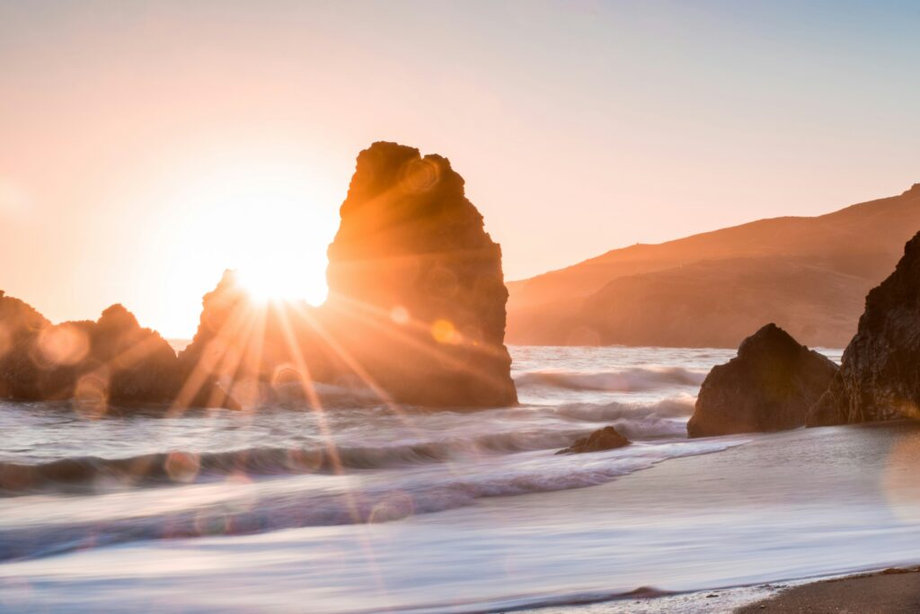 Sun rising behind rock formations on the beach.