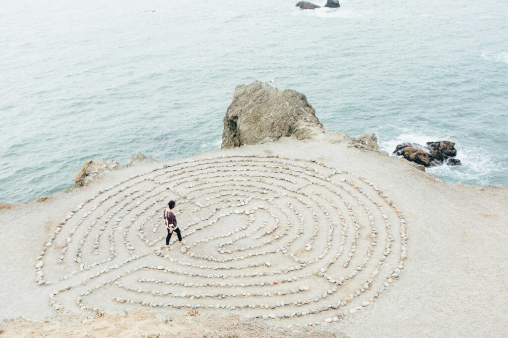 Person walking on the beach amidst a ritualistic stone labrynth.