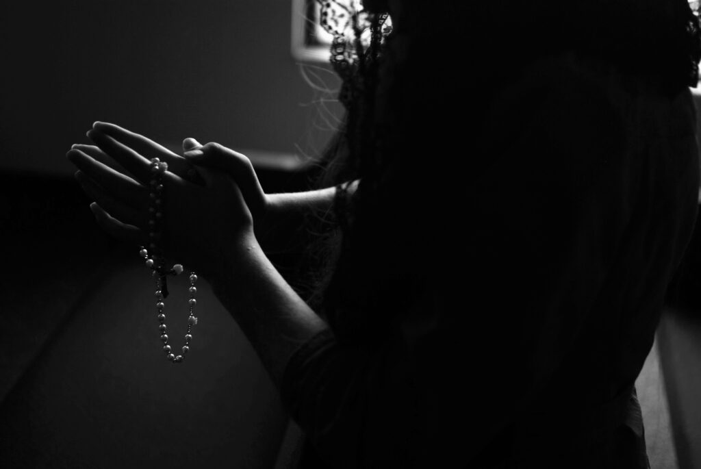 Person praying with mala beads in a dark room.